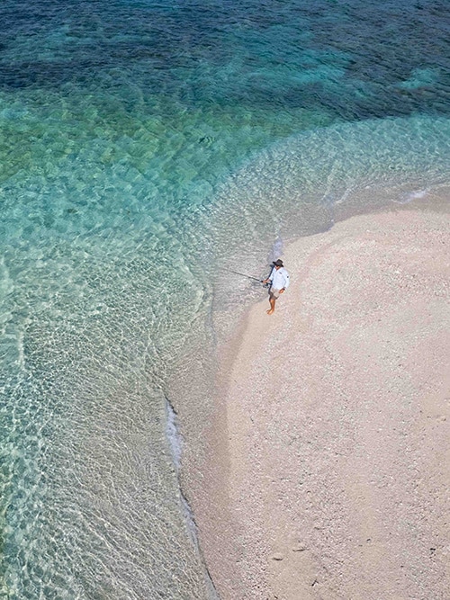 Man in linen shirt and shorts fishing on the white sand shores of Cocos Keeling Islands