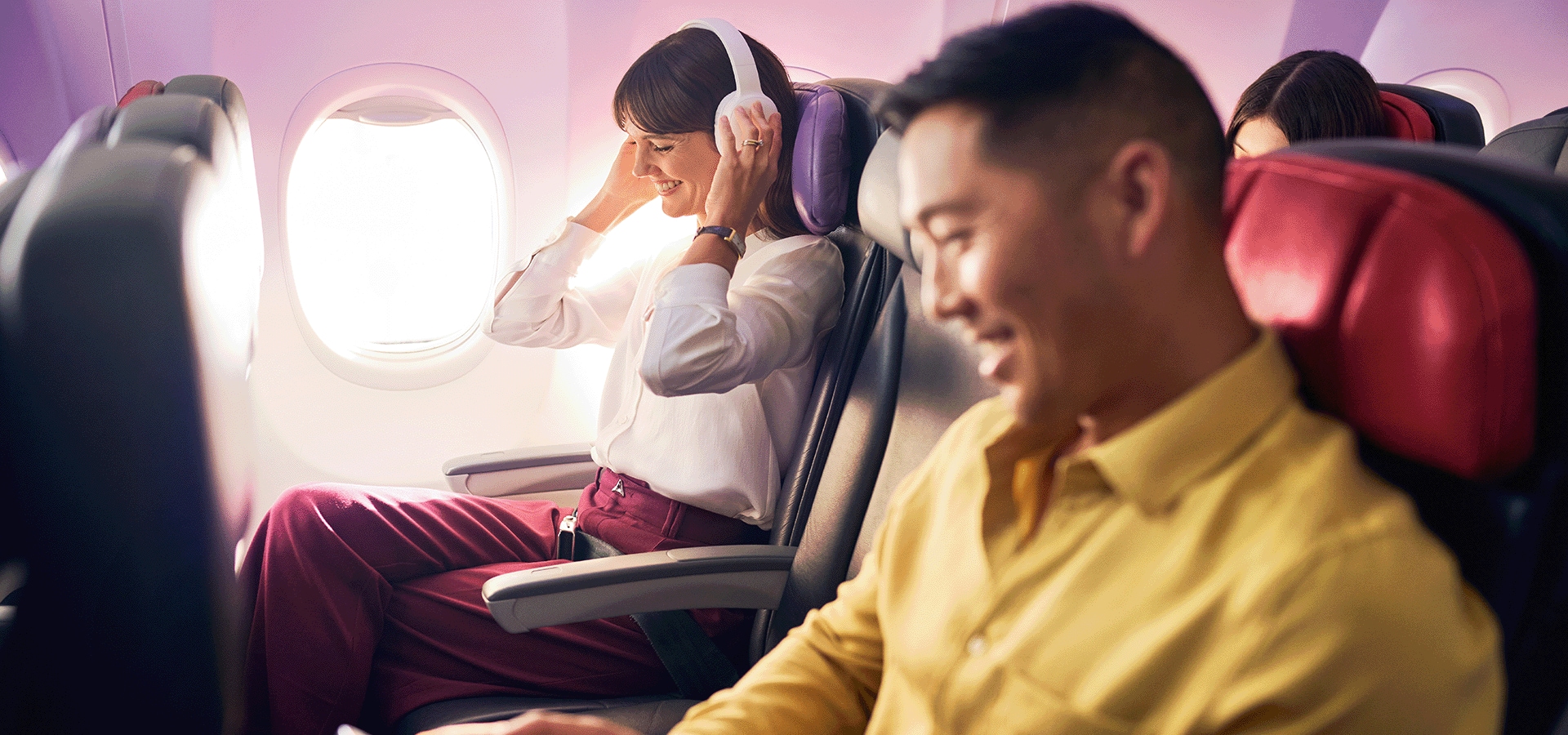Guests travelling on Virgin Australia flight sitting in cabin with headphones on listening to music.