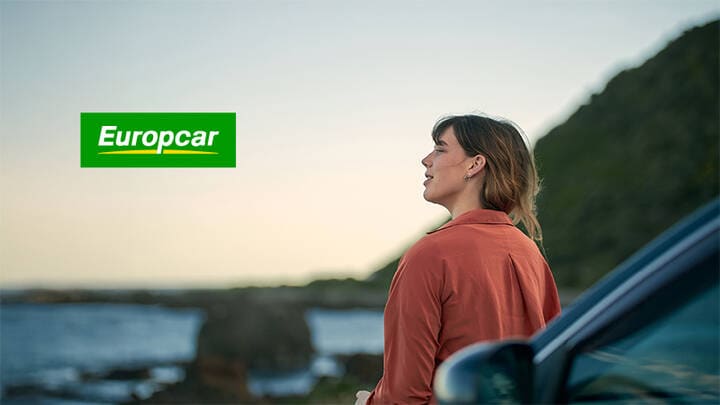 Woman looking out at beach scenery next to Europcar hire car.