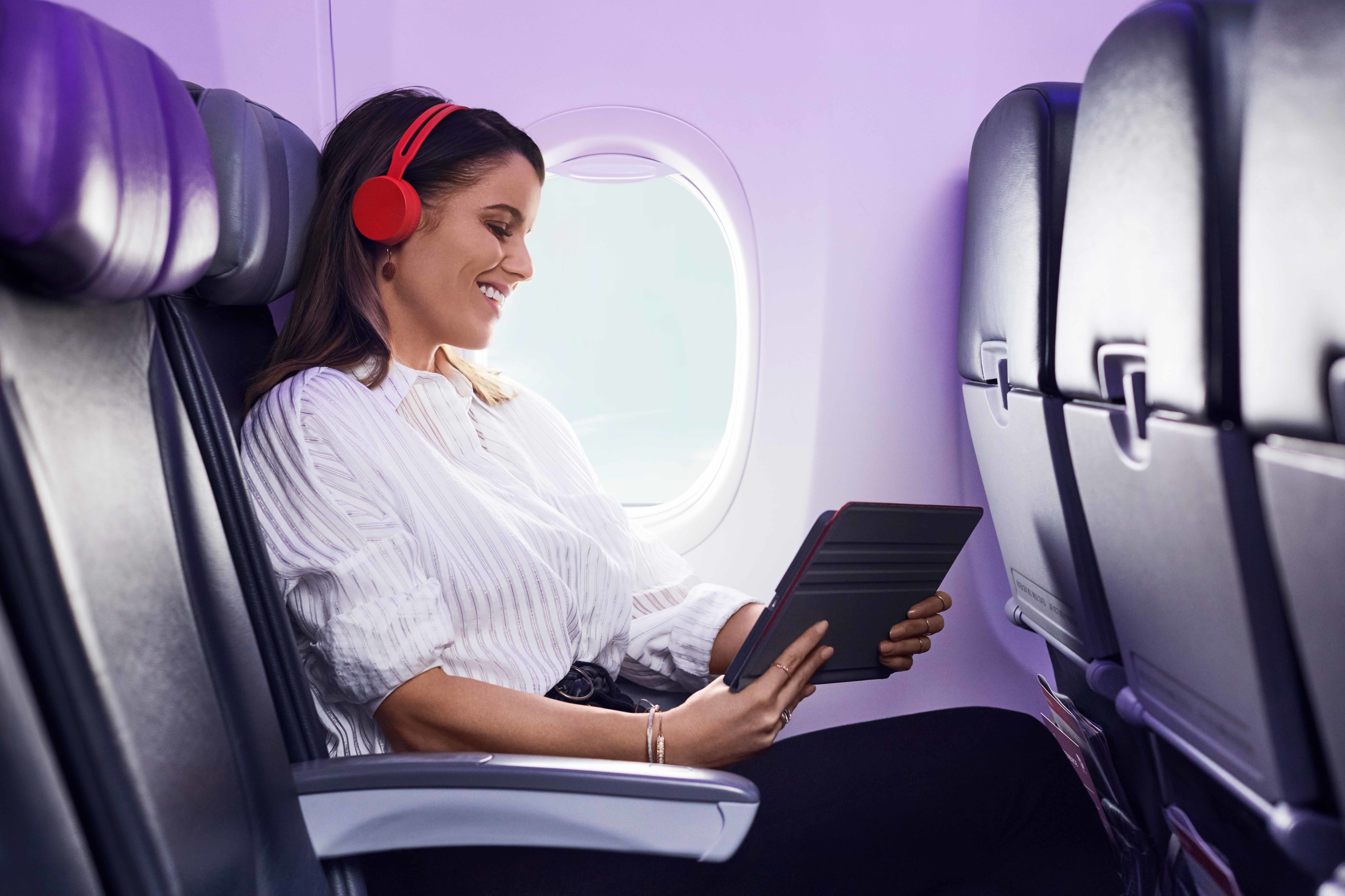 A passenger on a Virgin Australia flight enjoying in-flight entertainment on a personal device, relaxed and engaged in their content.