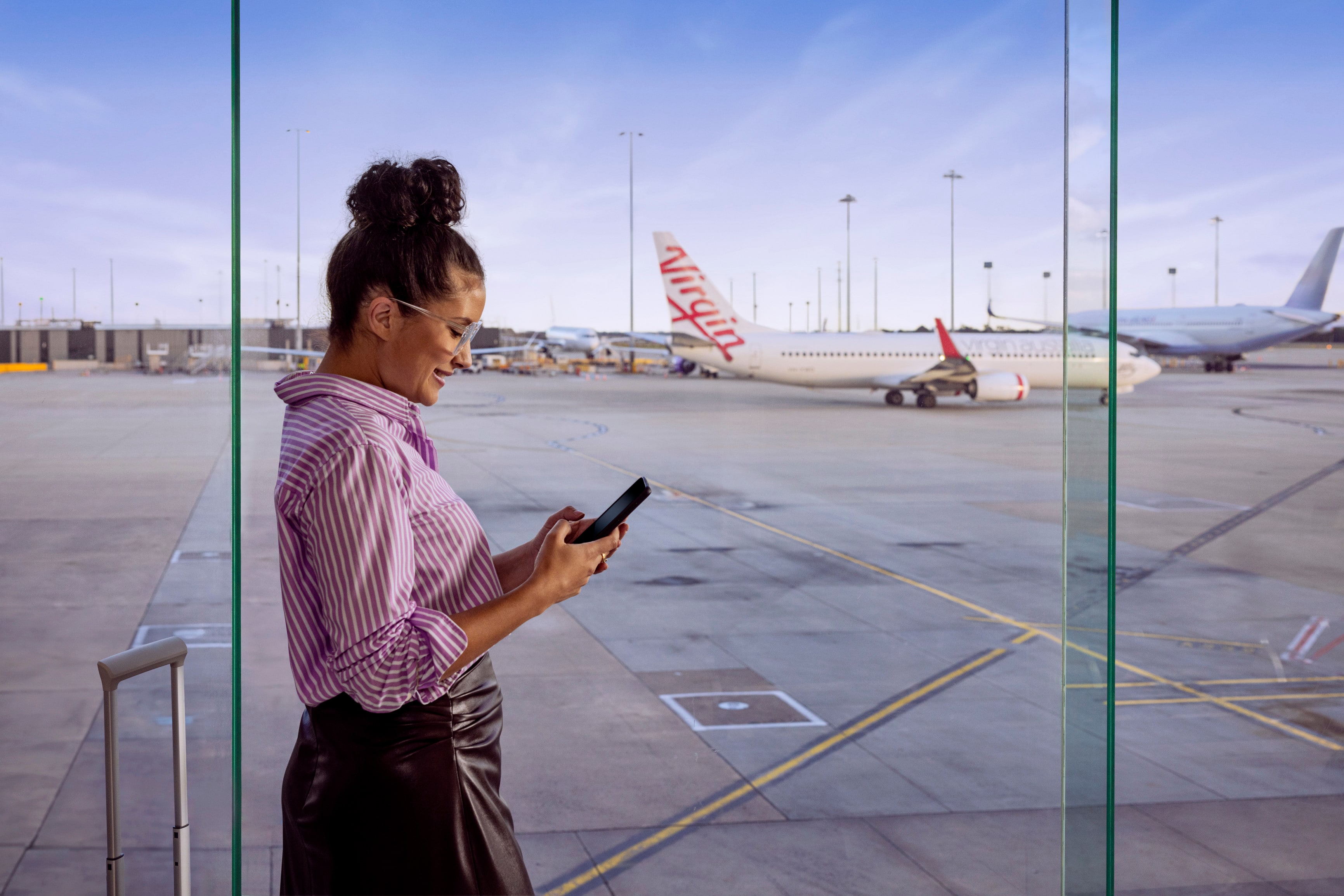 Business woman looking down on phone checking emails with aircraft in background on tarmac at Virgin Australia Lounge