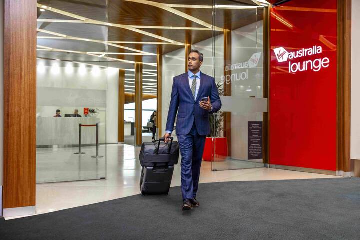 Business traveller exiting Virgin Australia Brisbane Airport lounge with suitcase cabin luggage