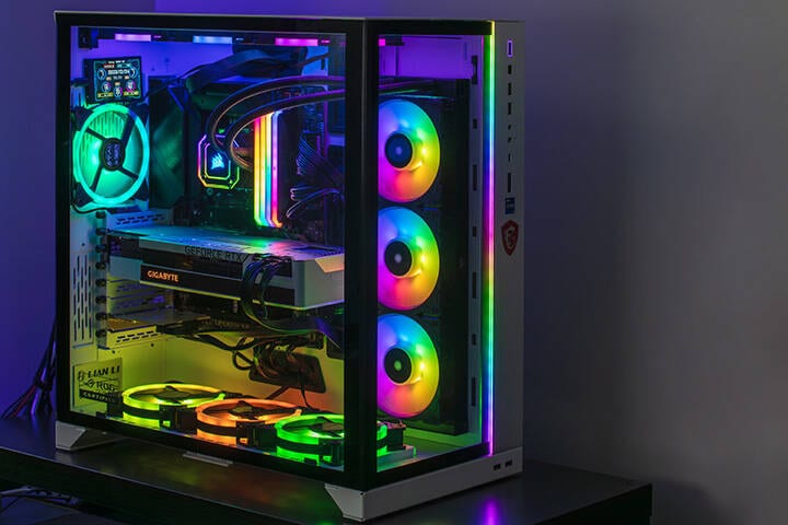 Close-up view of modern gaming PC in glass case with RGB glowing LED lights, CPU water cooling and NVidia GeForce RTX graphics card while working in dark room in MOD
