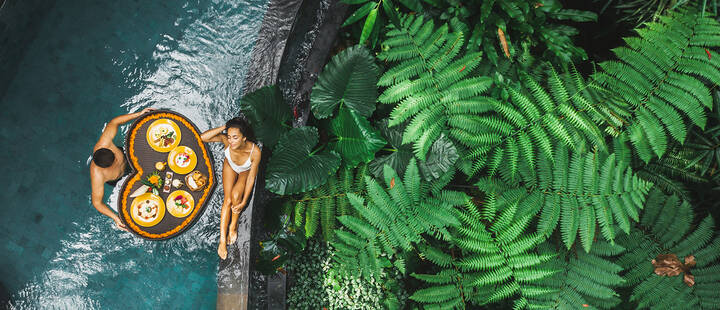 Couple in Bali eating floating breakfast in jungle swimming pool.