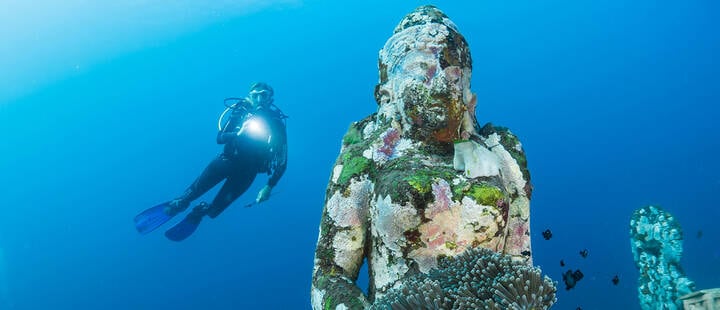 Diver diving on ocean floor near Buddha statue in Bali 