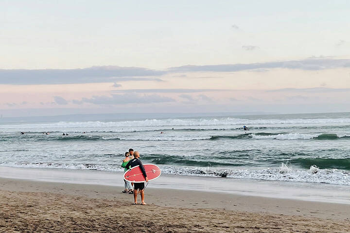 a couple of people walk on the beach carrying surfboards at Batu Bolong Beach 