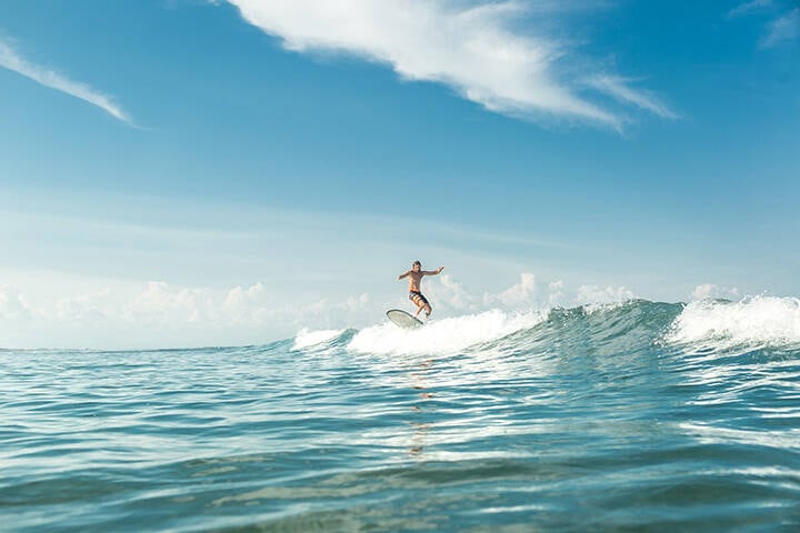 Distant view of male surfer riding waves at Nusa Dua Beach, Bali, Indonesia