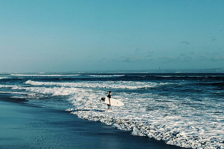 a person holding a surfboard walking into the ocean at Old Man's