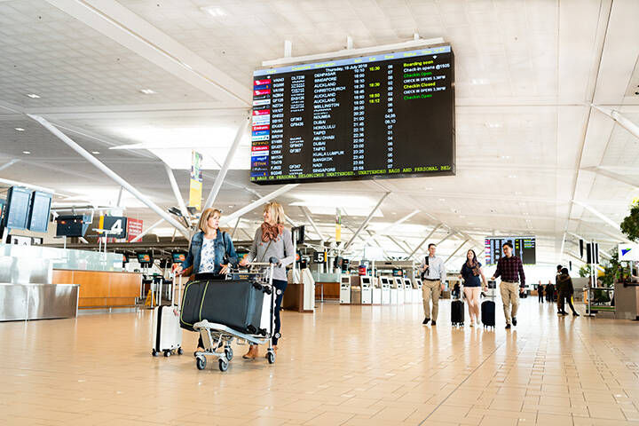 People walking at the Brisbane airport hall with their luggage 