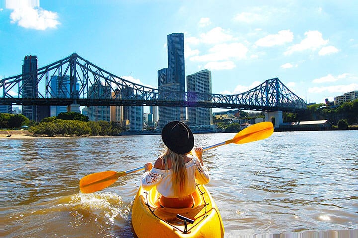 woman kayaks on the Brisbane River with Story Bridge in the background 