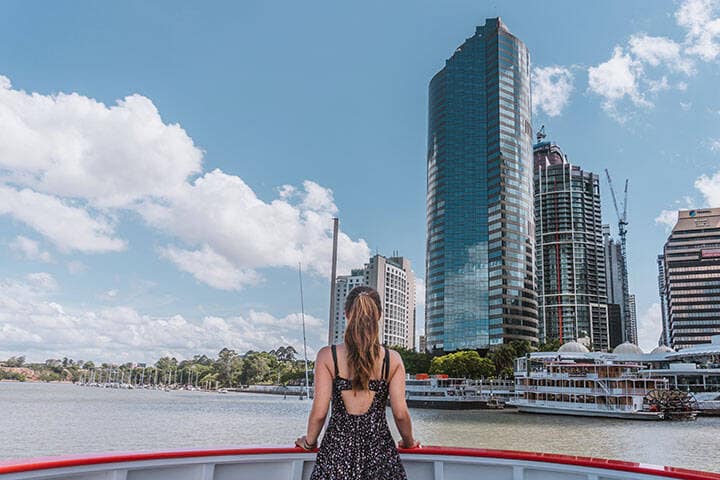 Woman with her back on the Brisbane River ferry, facing the tall buildings of the city's commercial centre