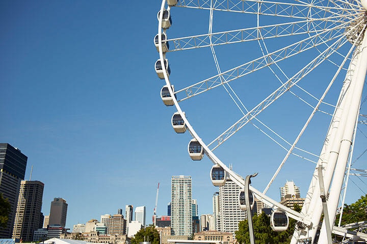 An image with Wheel of Brisbane taking half of the picture and cityscape and blue sky 