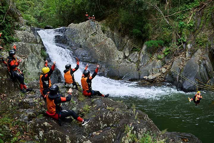 Tour group with hands up cheering and watching some of the group ziplining over Crystal Cascades