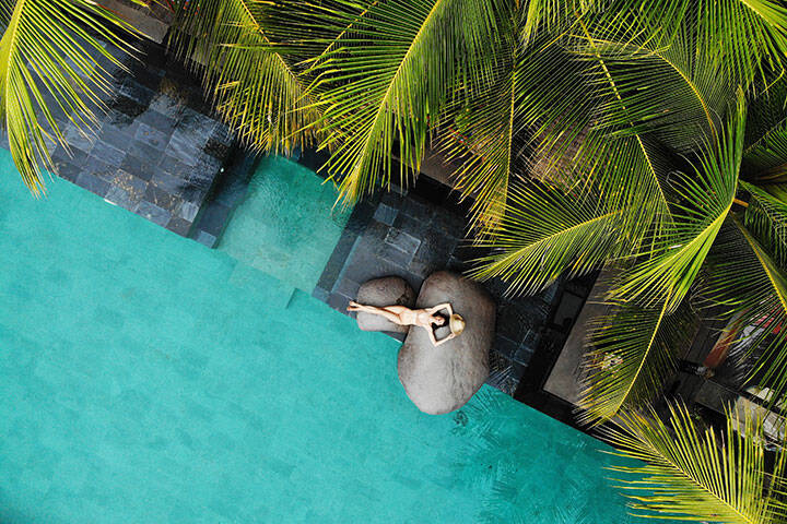 Aerial view of woman in a bikini relaxing at a luxury pool under palm trees