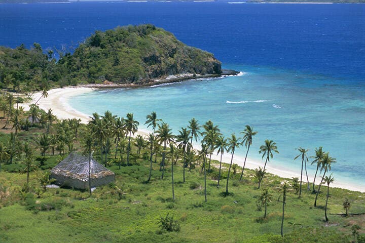 Coconut plantation and old farmhouse beside coral sand bay, Mana Island, Mamanuca group, west of Viti Levu, Fiji, South Pacific islands  