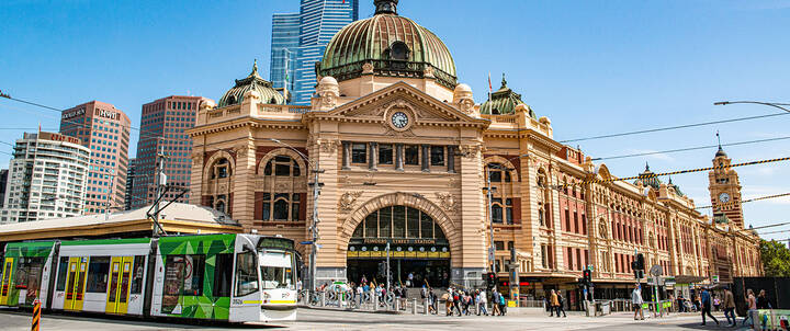The facade of Flinders Street Station in Melbourne, busy with pedestrians and trams. 