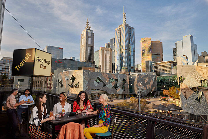 People enjoying rooftop drinks in Melbourne, with Federation Square and the city in the background.  