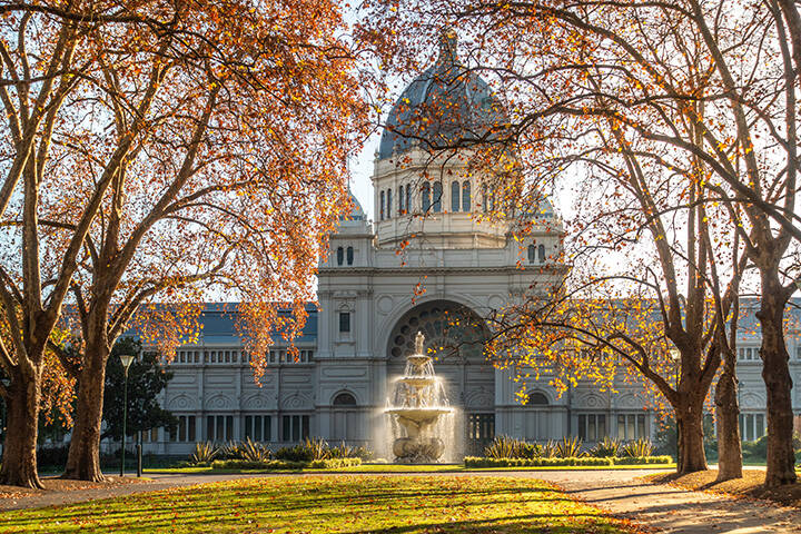 The historic Royal Exhibition Building and autumn trees bathed in morning sunlight in Carlton Gardens. Melbourne's local tourist attraction and sightseeing place with enchanting atmosphere of autumn