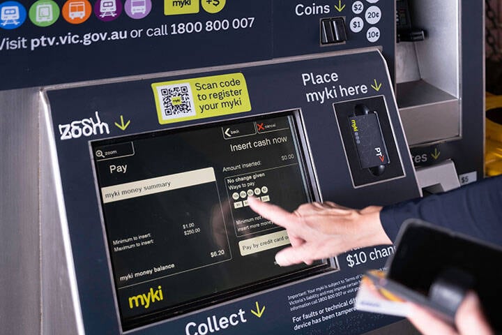 Woman loads her public transport mobility card at a Myki station machine in Melbourne