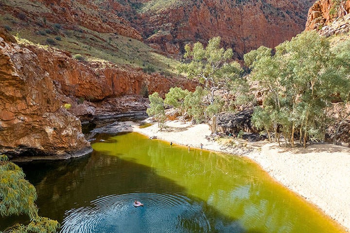 Swimming at Ormiston Gorge. Ormiston Gorge is located 135 kilometres west of Alice Springs in the West MacDonnell National Park, it is accessible via sealed roads and is the Trailhead for sections 9 and 10 of the 231 kilometre Larapinta Trail walk.  The gorge has a near-permanent waterhole that is ideal for swimming, especially in the warmer months. Just 500 metres from the visitor centre, it is estimated to be up to 14 metres deep at its southern end.