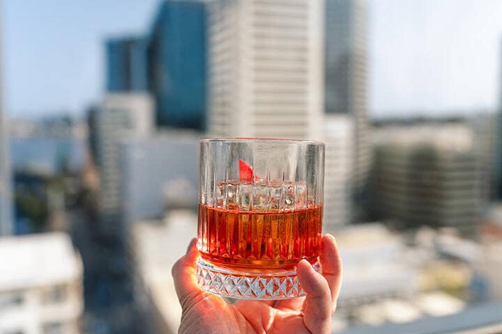 Holding a negroni cocktail overlooking the city at a rooftop bar in Perth, Australia
