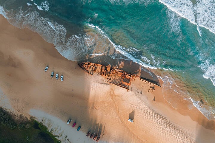 High angle aerial bird's eye drone view of the Maheno shipwreck on Seventy-Five Mile Beach on K'Gari (Fraser Island), Queensland, Australia. Beautiful sunset light with waves.
