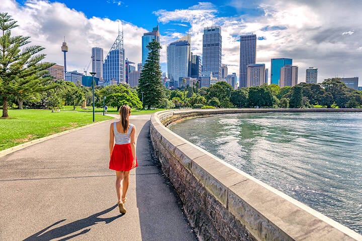 Tourist walking through Botanic Gardens in Sydney city, with skyscrapers skyline in the background on a cloud day