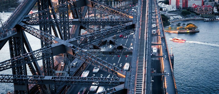 Cars driving over the Sydney Harbour Bridge at sunset
