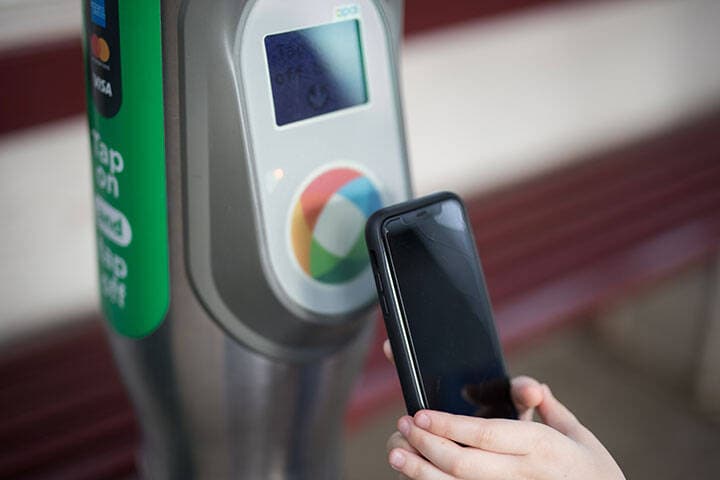 Traveller tapping their phone on an Opal card reader to use the contactless payment for their public transport fare. 