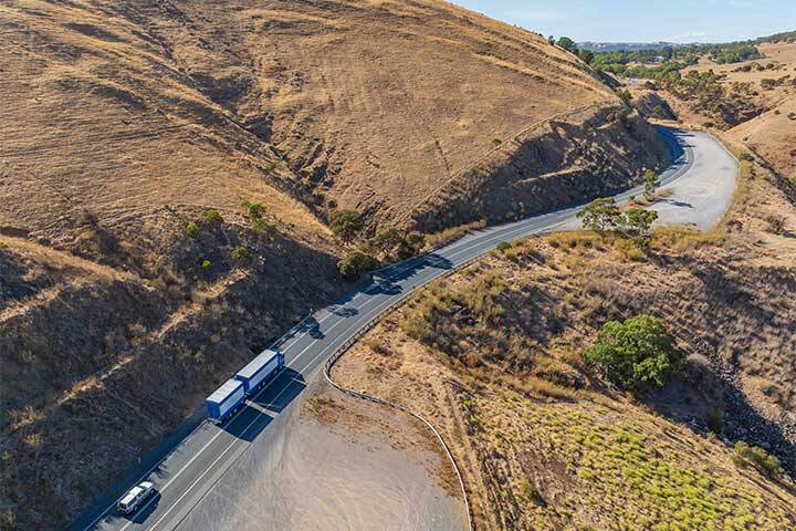 Aerial view of trucks and cars travelling up a mountainside road through a cutting