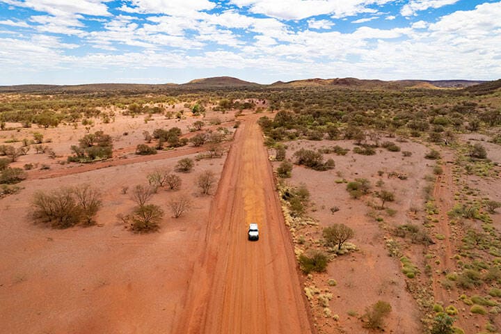 Car driving down dusty red road in Pilbara