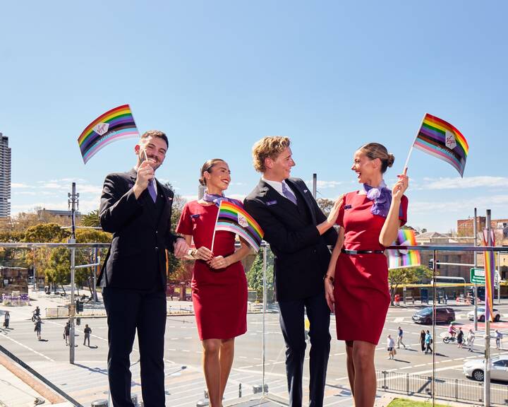Four flight attendants waving rainbow flags on a balcony 