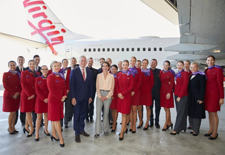 CEO of Virgin standing with cabin crew in front of plane in hangar