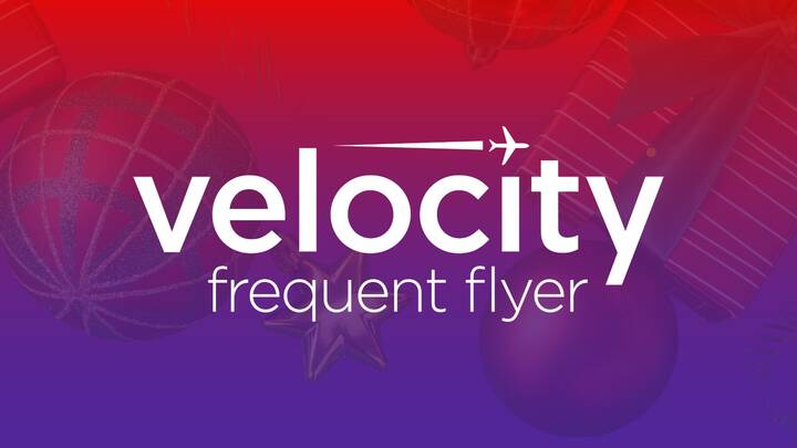 Velocity Frequent Flyer logo in white on a red-to-purple gradient background with Christmas ornaments and wrapped gifts faintly visible behind the text.